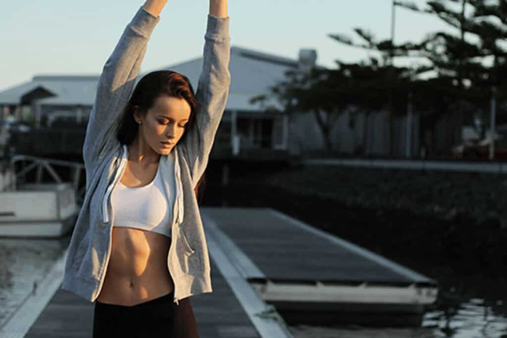 woman stretching with her hand in the air in active clothing outdoors