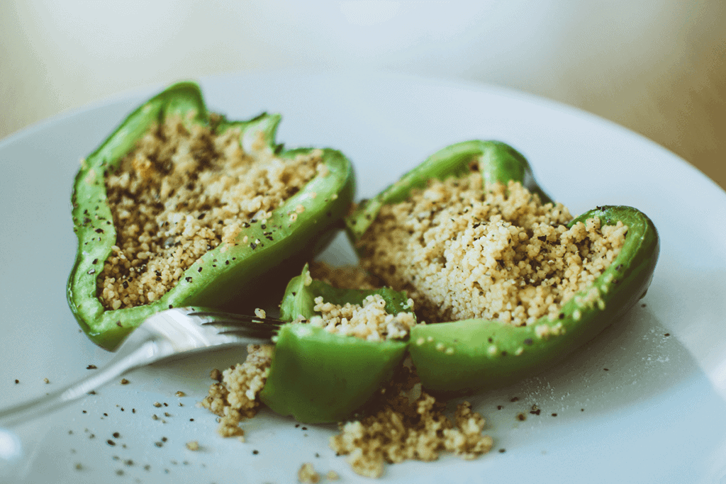 green pepper cut in half with quinoa inside on white plate with a fork