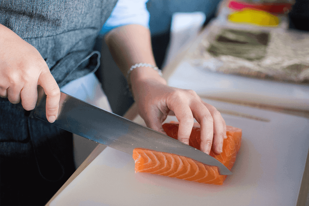 person cutting a piece of salmon into multiple pieces for cooking