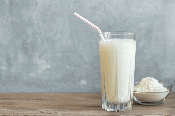 vanilla milk based drink with whey protein powder next it in a glass bowl