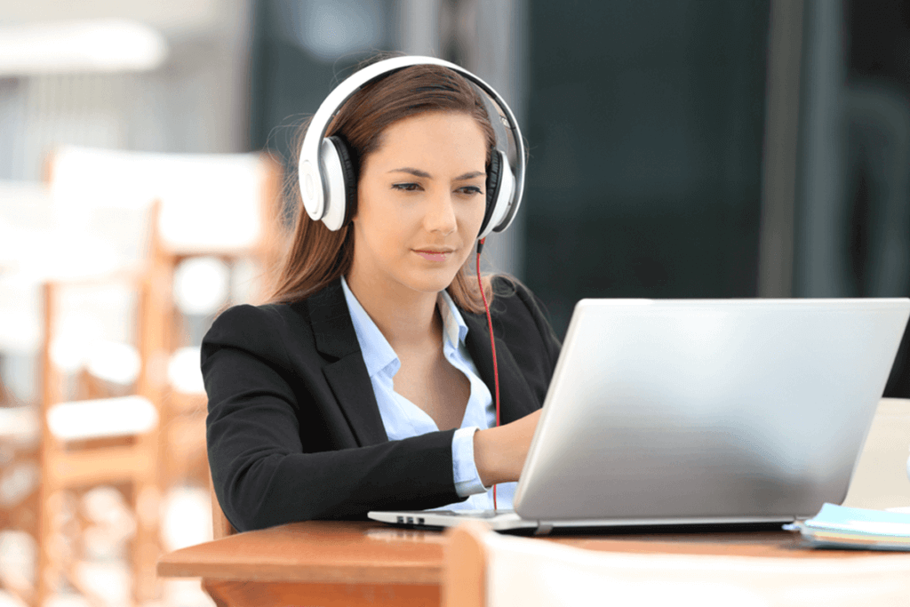 woman with headphones on looking at her laptop screen while sitting