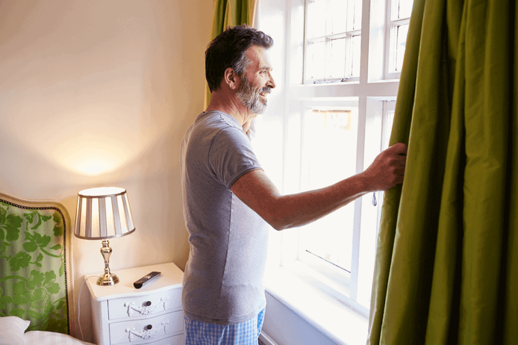 man looking out his bedroom window in pjs looking at the sunrise