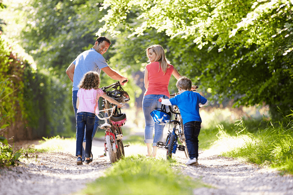 family of four pushing their bikes outside in a forest area