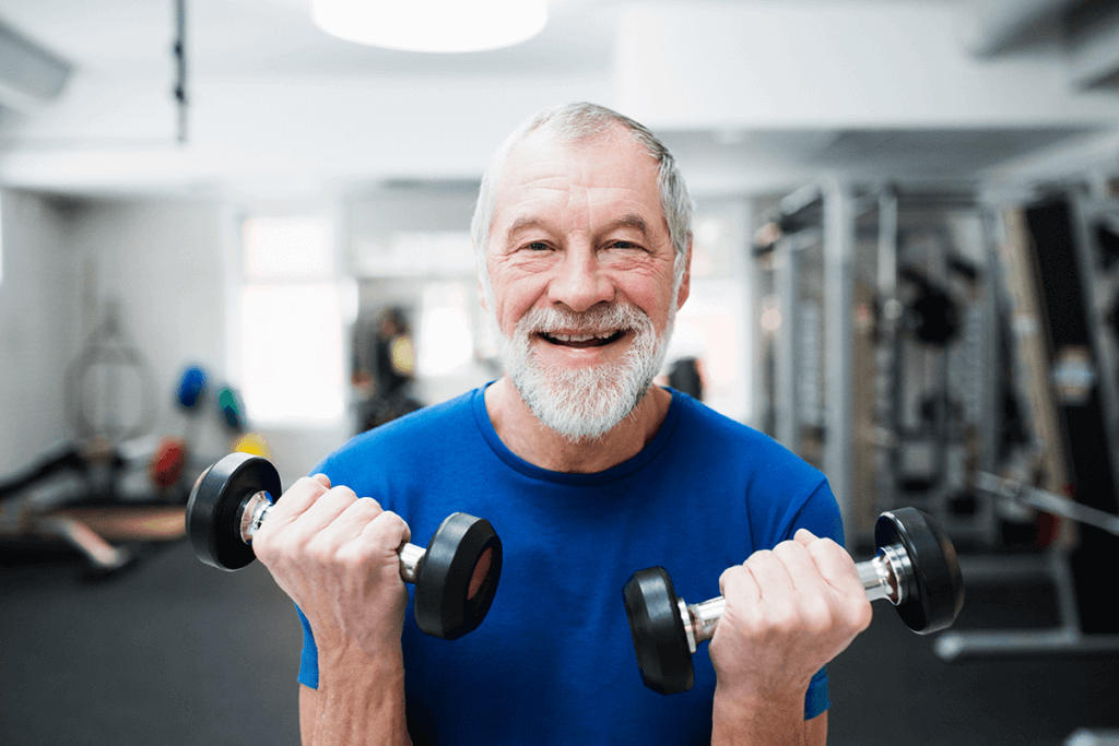 older man lifting dumbbells at gym smiling into the camera