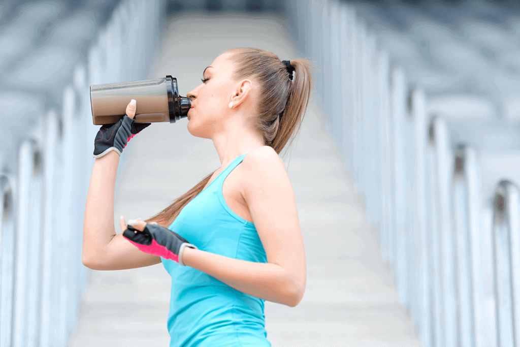woman in active wear drinking protein from plastic bottle