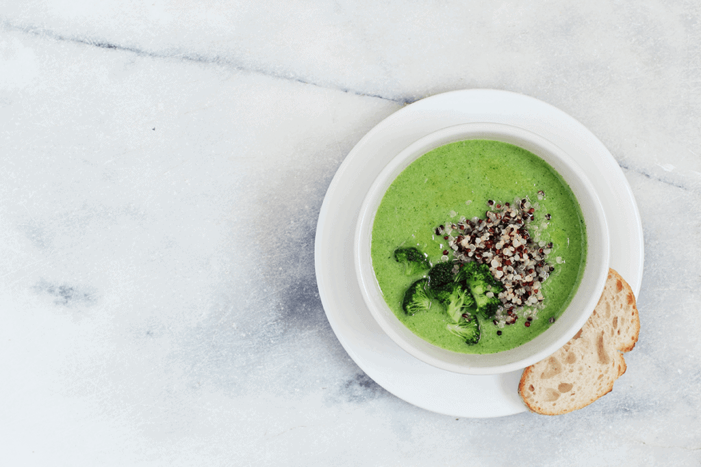 healthy green soup in a white bowl with slide of bread next to it overview look