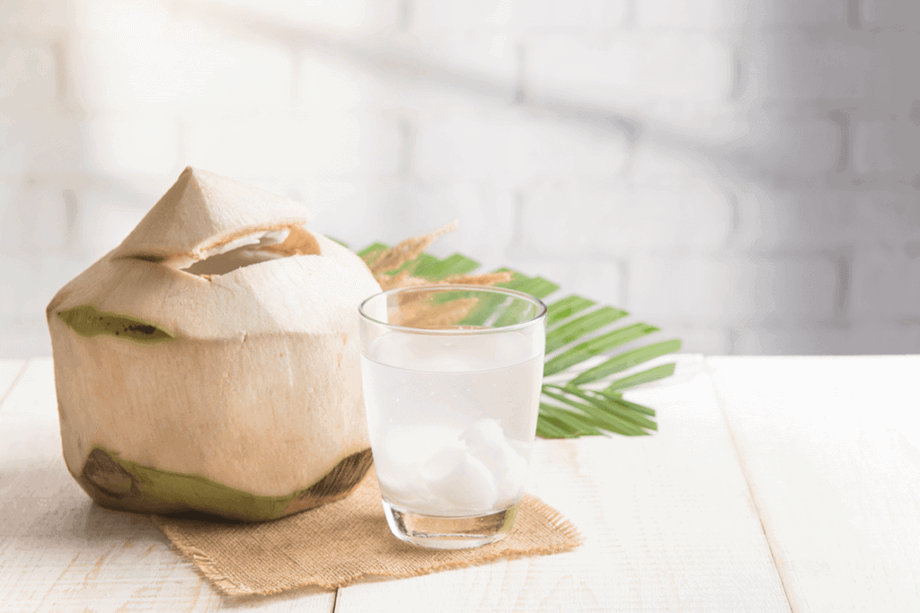 raw coconut cut up next to a glass of coconut water