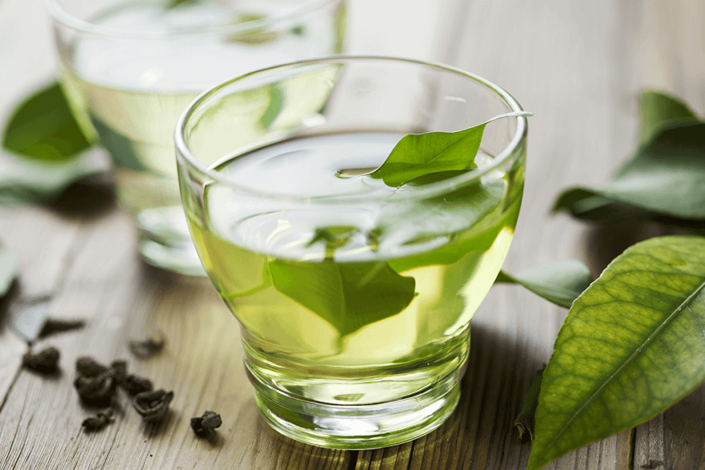 Green tea in clear glass with green tea leaves on wooden table