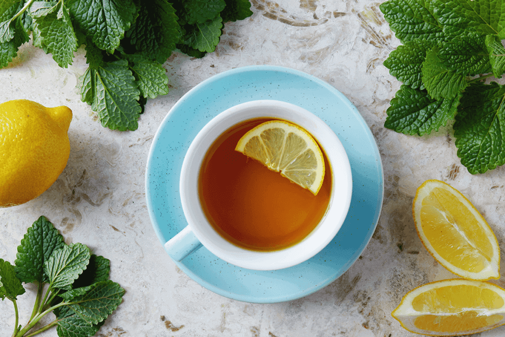 A blue tea cup full of lemon tea with slices of lemon next to it.