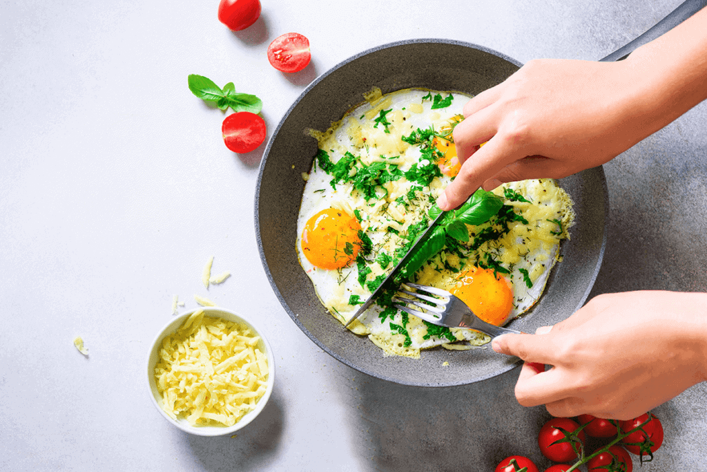 Two hands preparing eggs in a pan with cheese and tomatoes