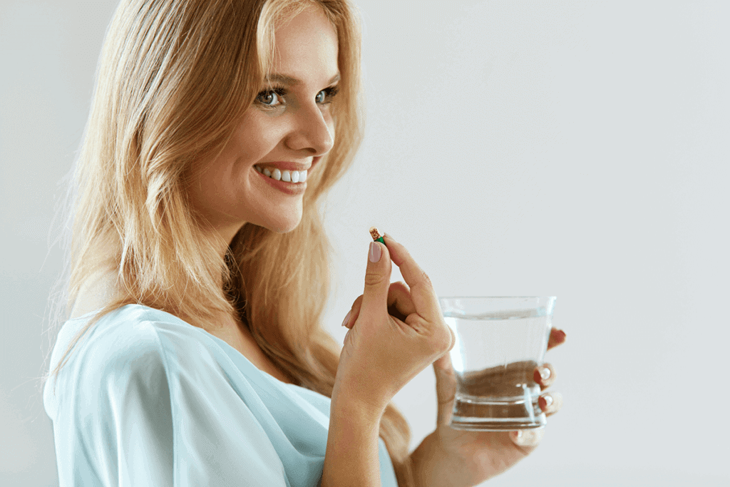 woman taking a supplement holding water