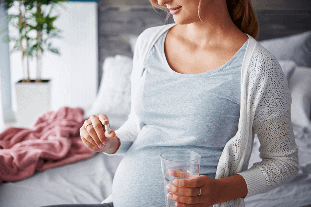 pregnant woman holding a supplement and a glass of water