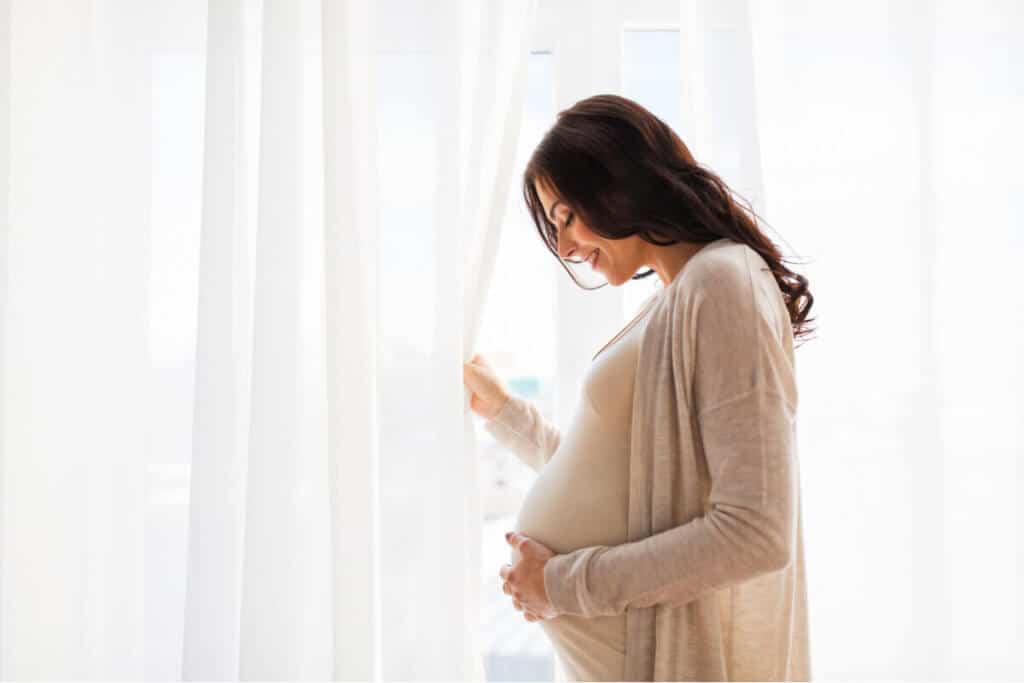 Pregnant woman holding her stomach beside a sunlit window