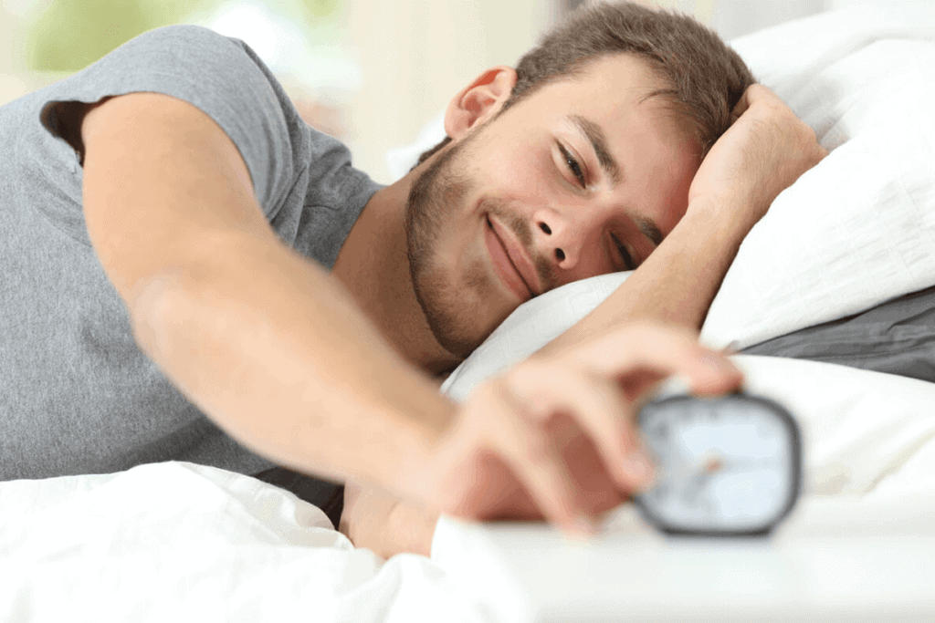 man in bed reaching out for his alarm clock