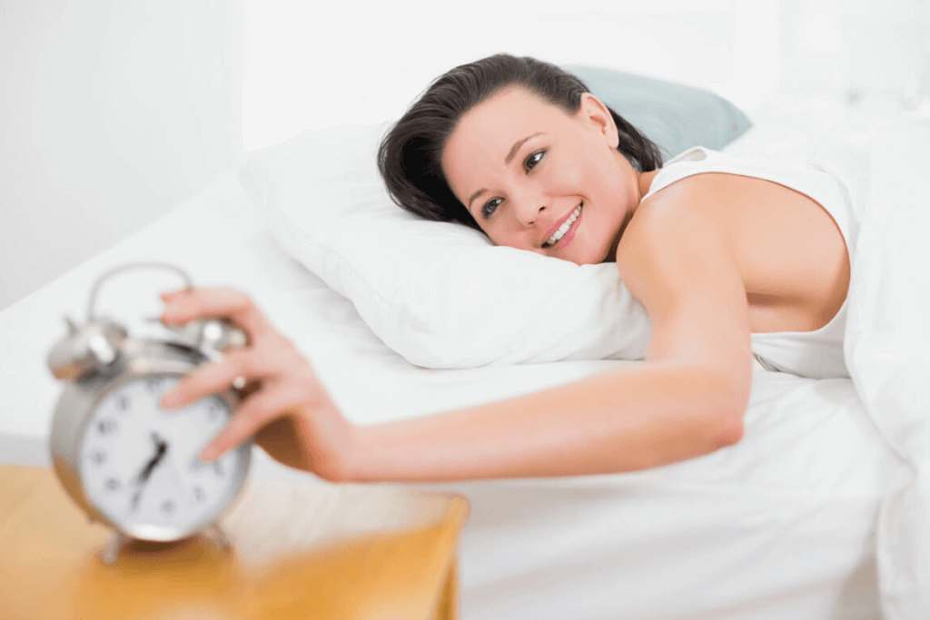 woman in bed hitting her alarm