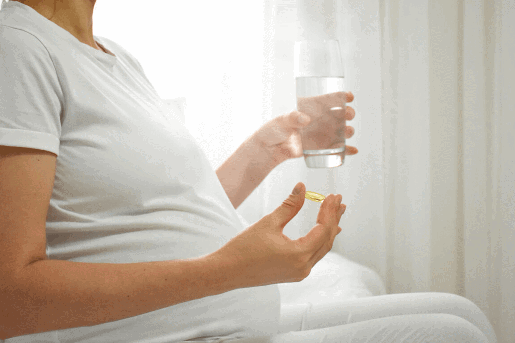 pregnant woman holding a glass of water and a fish oil supplement pill