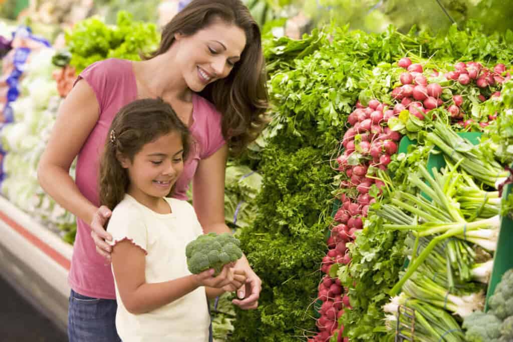 mother and daughter at grocery store picking up vegetable