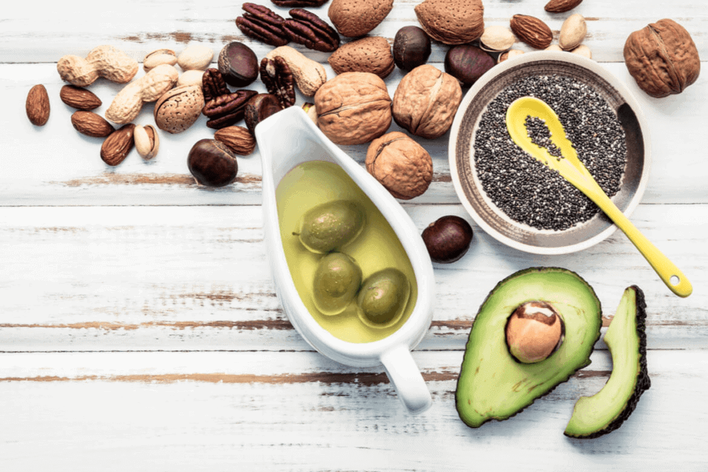 Flat-lay of nuts, avocado, olives in olive oil, and softgel capsules on a wooden table.