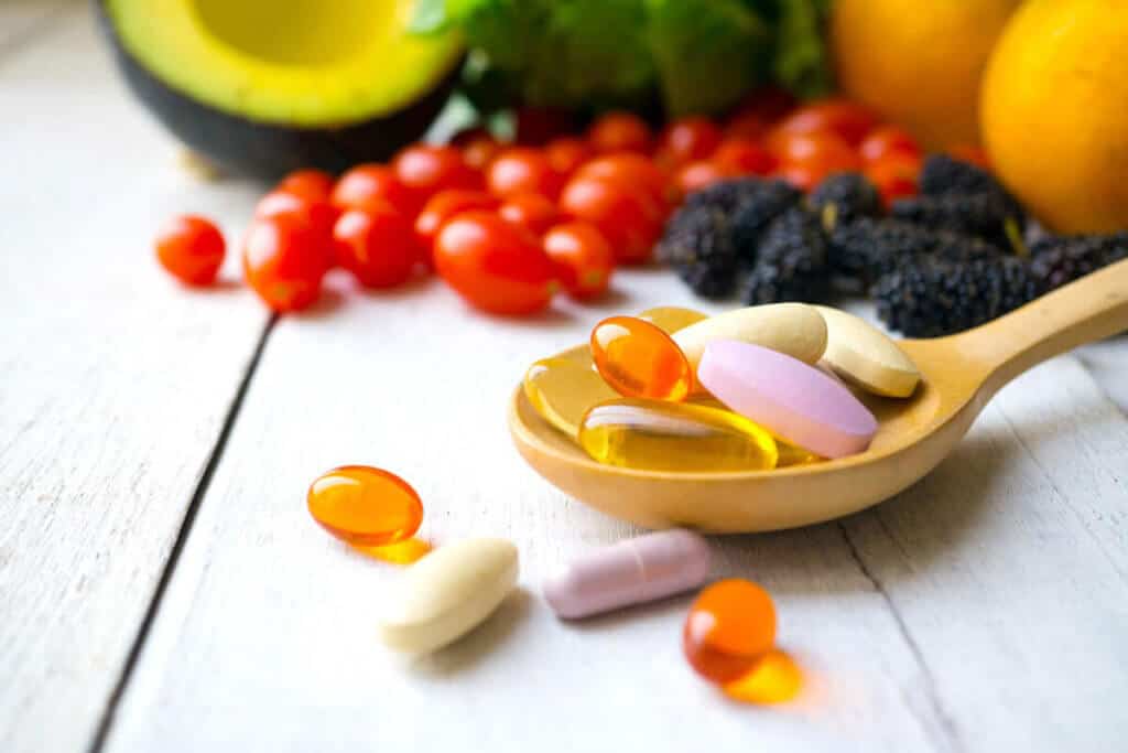 multivitamins on a wooden spoon with fruits in the background