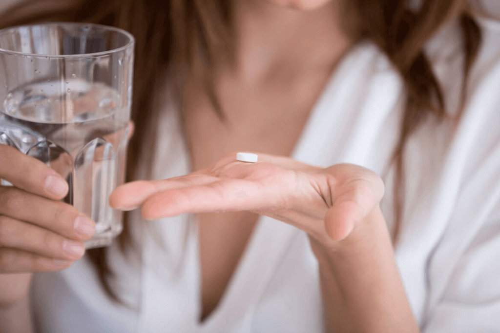 close up of woman's hand with supplement pill on it and water in the other hand