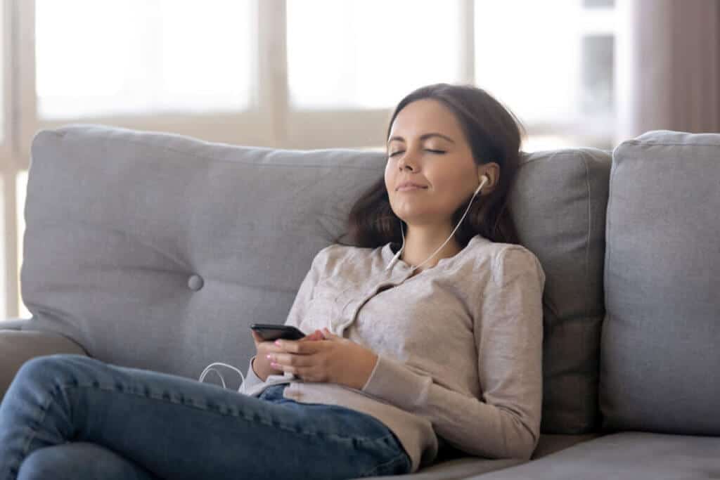 Young woman sitting on a sofa with headphones and eyes closed.