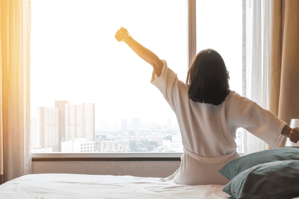 Woman sitting on a bed stretching while looking out of the window.