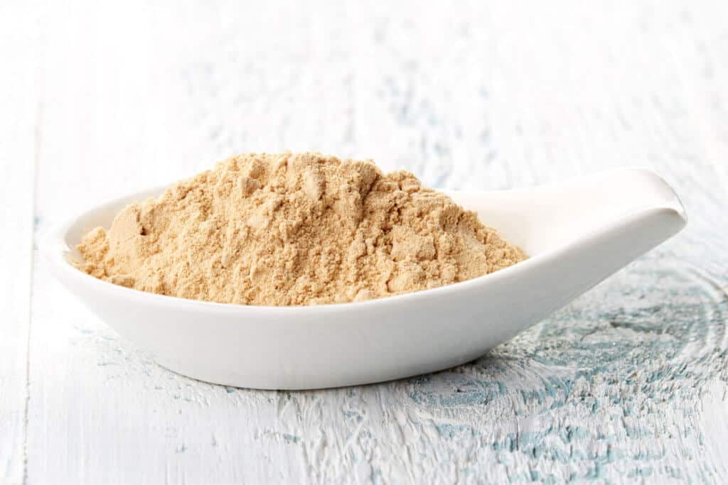 Maca powder in a spoon on a white table.