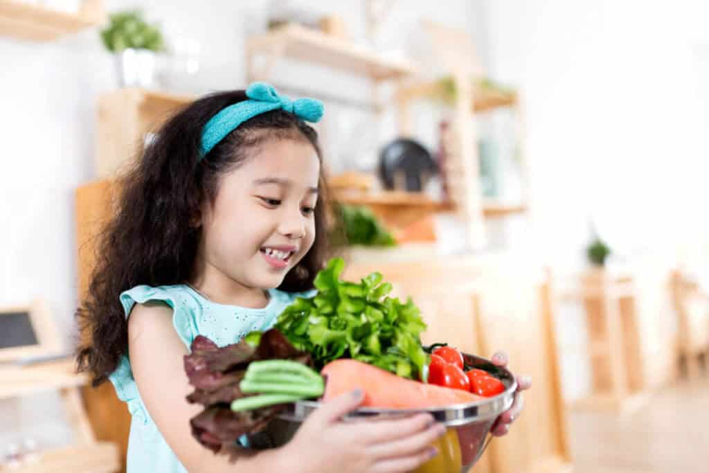 Young girl holding a bowl of vegetables and smiling.
