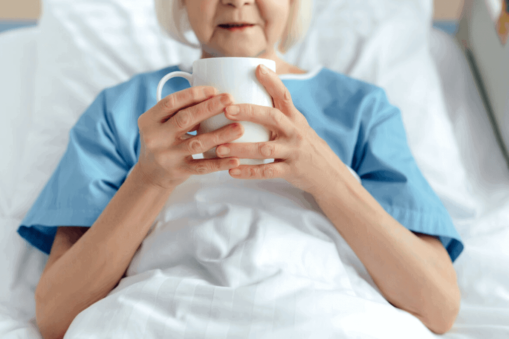 woman laying in hospital bed drinking tea from a white mug