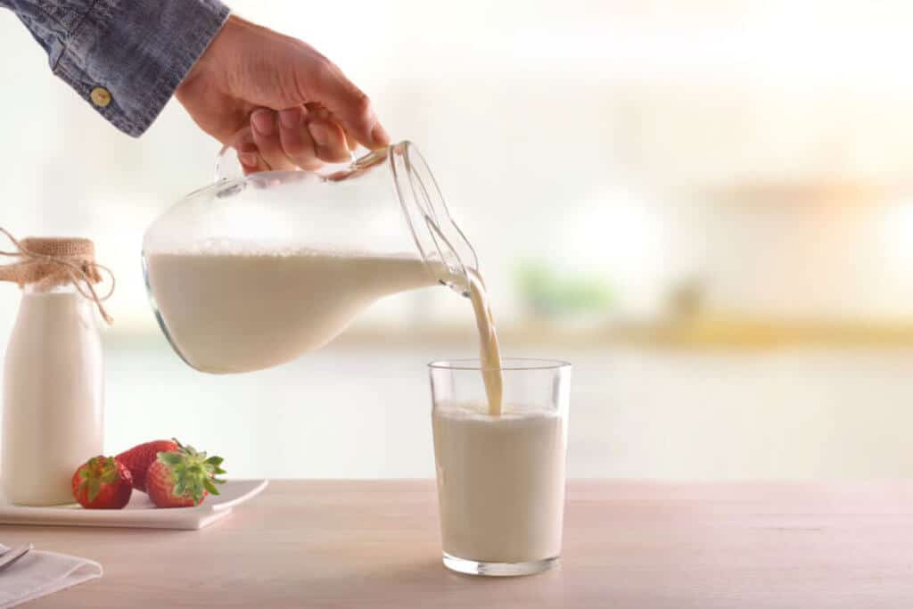 person pouring milk from jug into glass