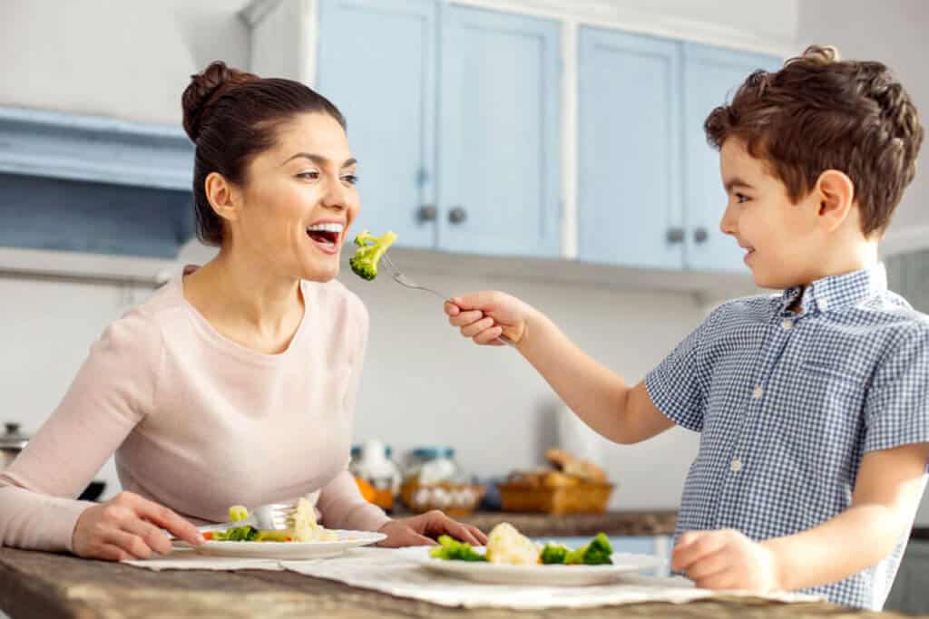 child feeding his mother a piece of broccoli