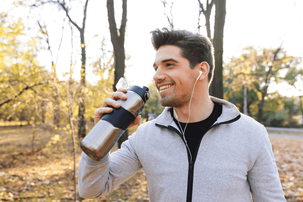 man running outside with headphones in and drinking water