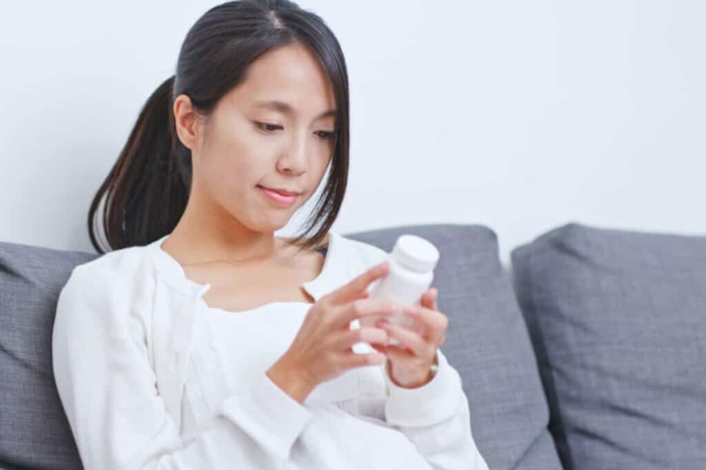 Young woman sitting on a sofa reading a supplement label.
