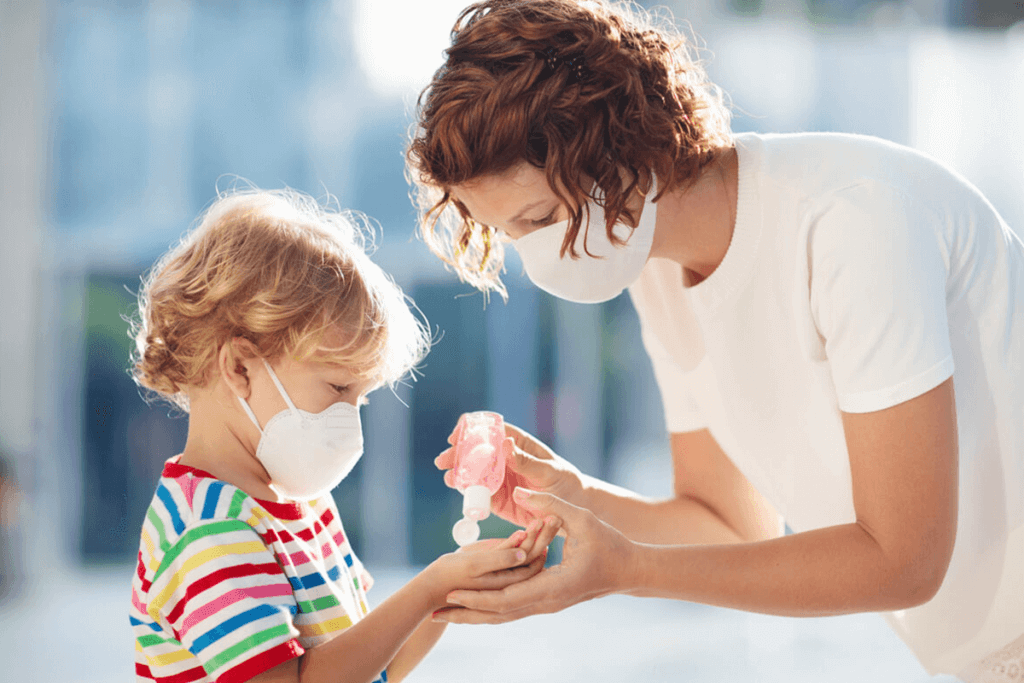 woman and child with face masks applying hand sanitizer to their hands