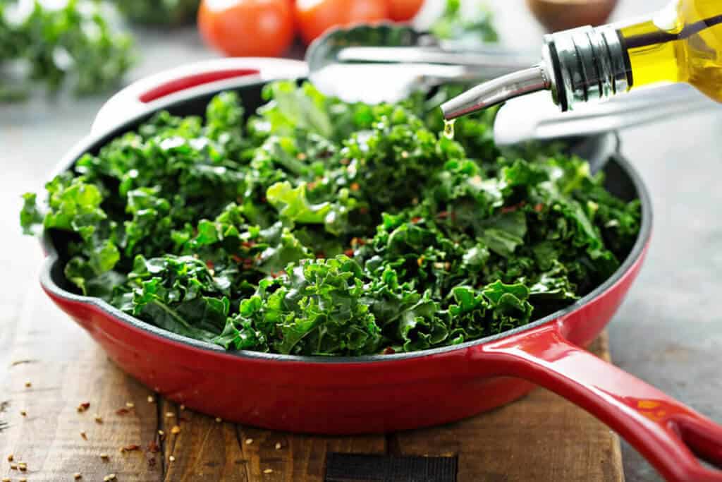 kale in a pan with oil being sprinkled on it