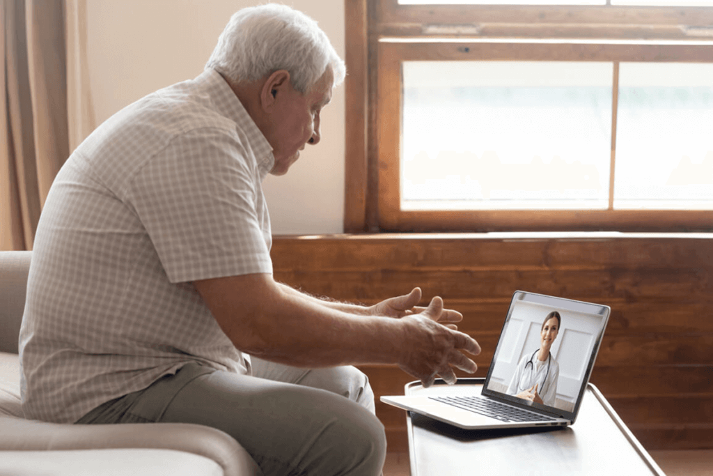 older man talking to healthcare practitioners on video chat through his computer, at home