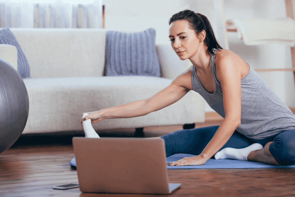 woman looking at her laptop in her living room stretching before a workout