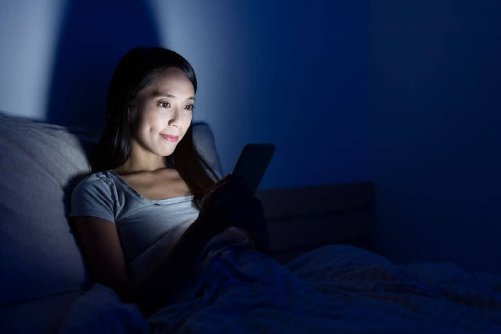 woman in bed at night looking at her phone, phone light illuminating her face