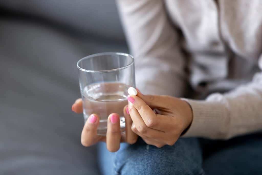 Image of woman holding a pill and a glass of water