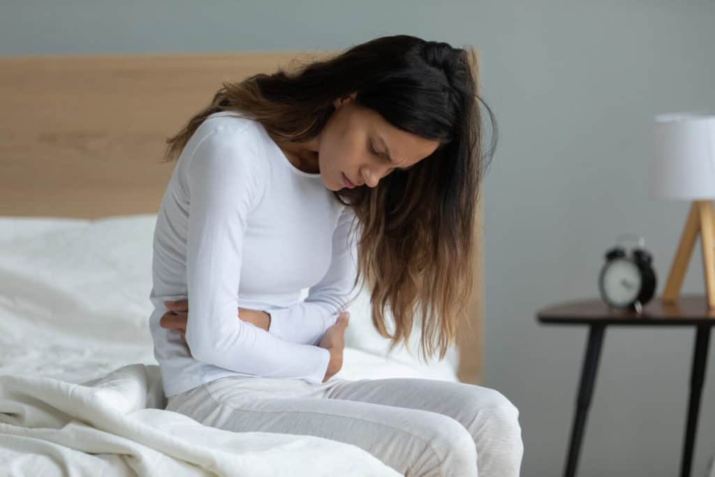 woman sitting on her bed holding her stomach in discomfort