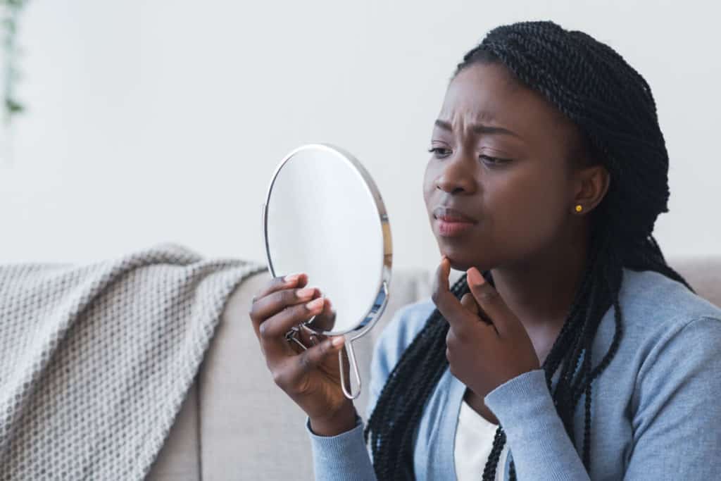 woman looking at her face in worry in a hand held mirror