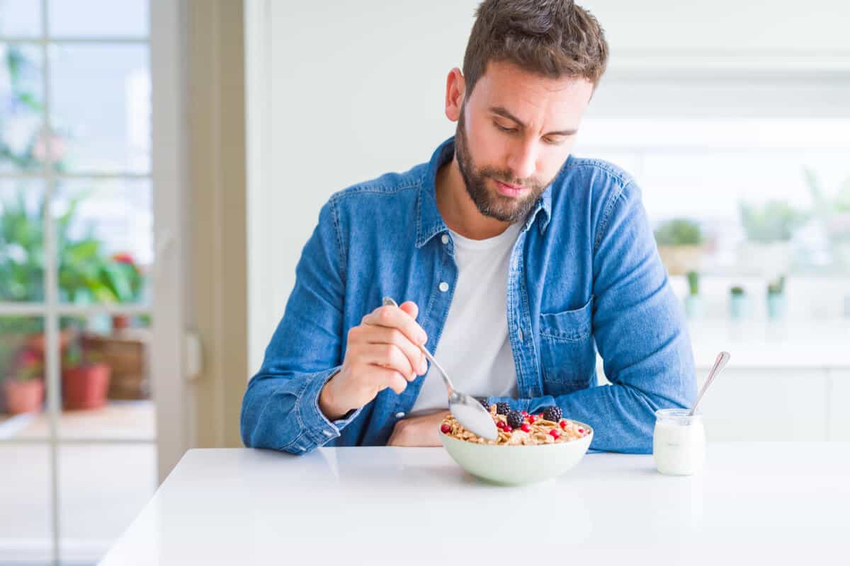 man sitting at kitchen table eating a bowl of yogurt with oats and berries
