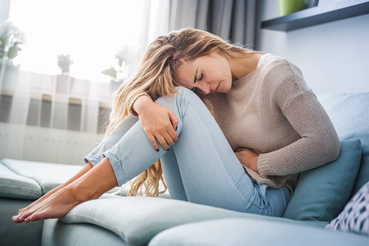 woman sitting on couch and holding her stomach in pain