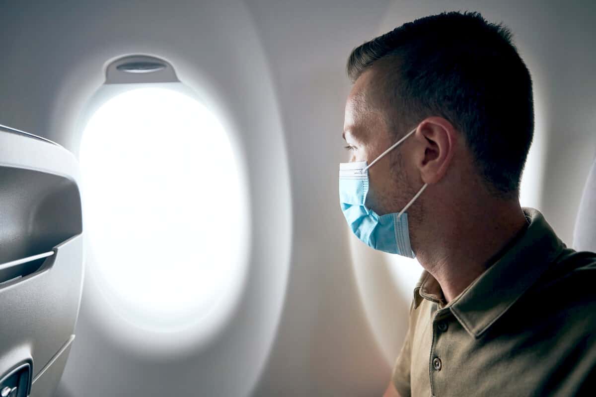 Man wearing a mask looking out the window of a plane