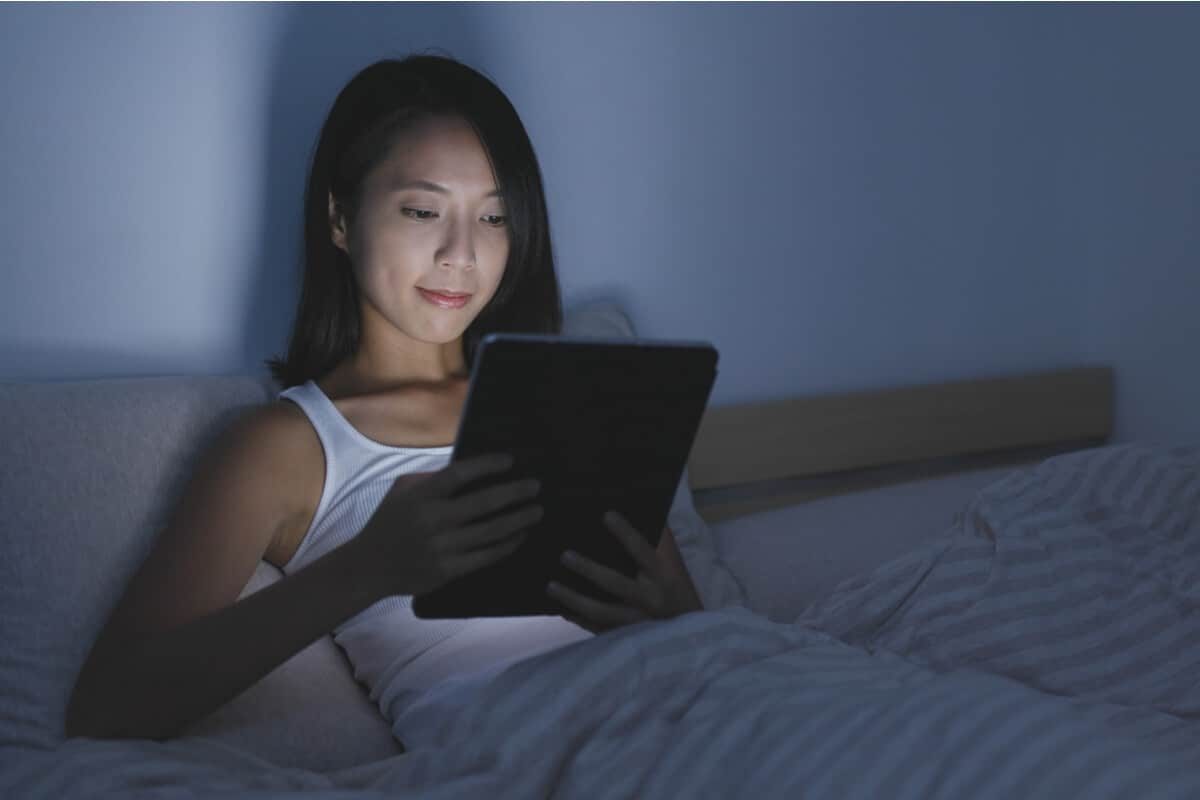 Woman lying in bed looking at a tablet screen