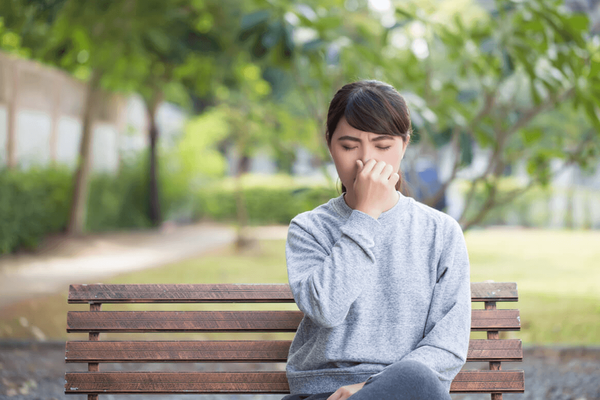 woman sitting on bench outside holding her nose