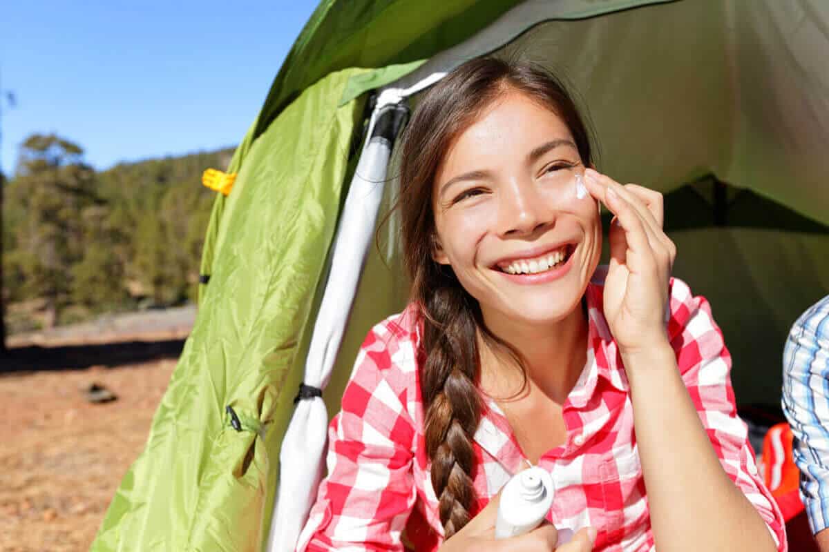 woman applying sunscreen on her face sitting in a tent