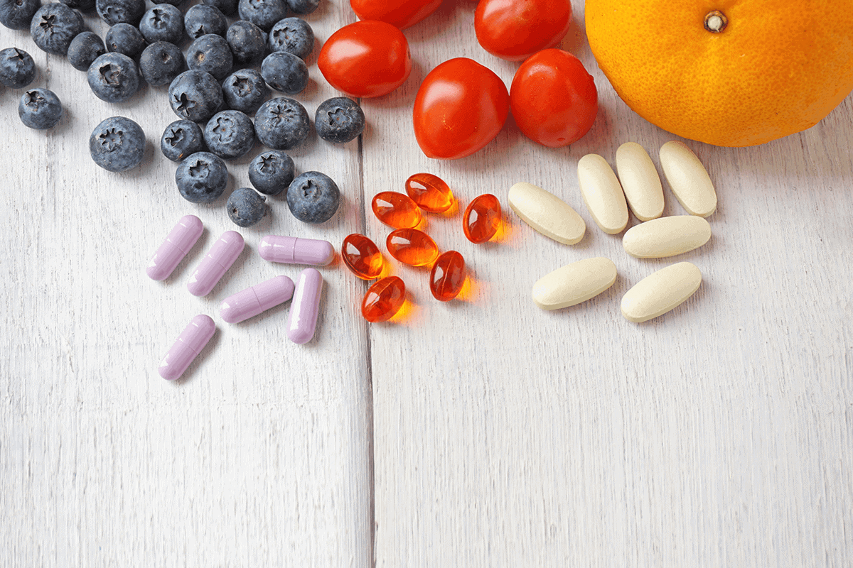 orange, tomatoes, and blueberries next to supplement capsules, and softgels