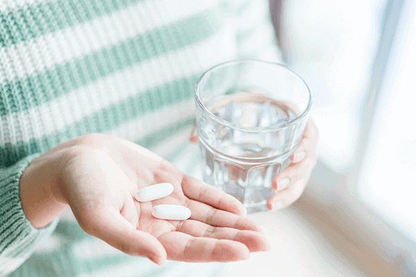 zoomed in on woman's hands one holding supplements in one hand and water in the other hand