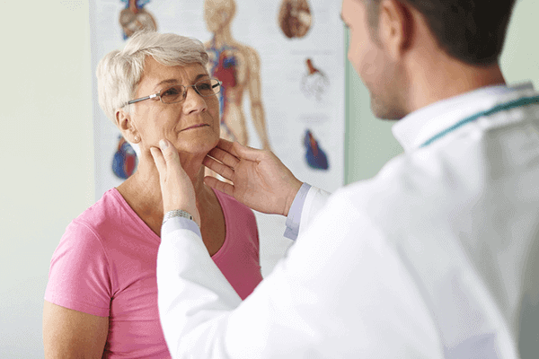 male doctor examining elderly woman's thyroid in doctor office